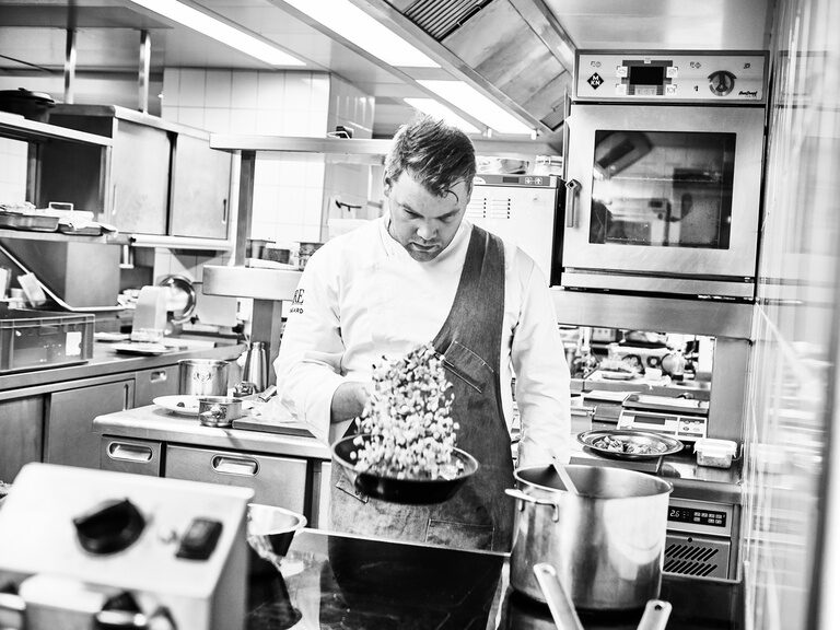 Franz Berlin und sein Team vom Gourmetrestaurant Berlins Krone servieren genussreiche, saisonale und regionale Spezialitäten auf höchstem Niveau. Ein Koch schwenkt gekonnt eine Pfanne mit Gemüse in der Restaurantküche des Hotel Kronelamm im Schwarzwald