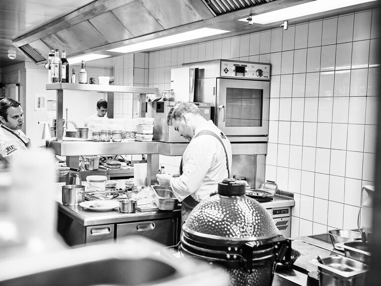 Franz Berlin bietet zusätzlich zu den Restaurantzeiten verschiedene Events wie Kochkurse an. In einer Restaurantküche arbeiten drei Köche zwischen diversen Kochutensilien und Lebensmitteln.