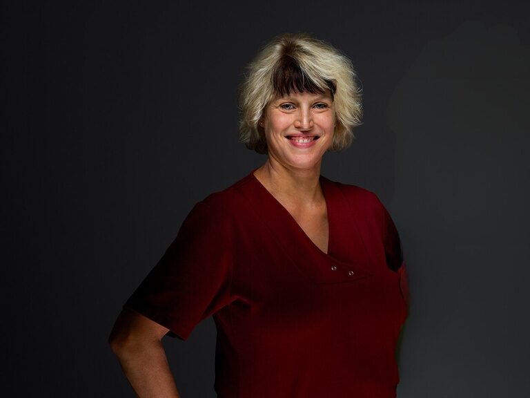 Vanessa Berlin, Frau von Roland Berlin leitet den Wellnessbereich königSPA Physiotherapeutin Vanessa Berlin lächelt bei einem Portraitfoto vor dunklem Hintergrund.